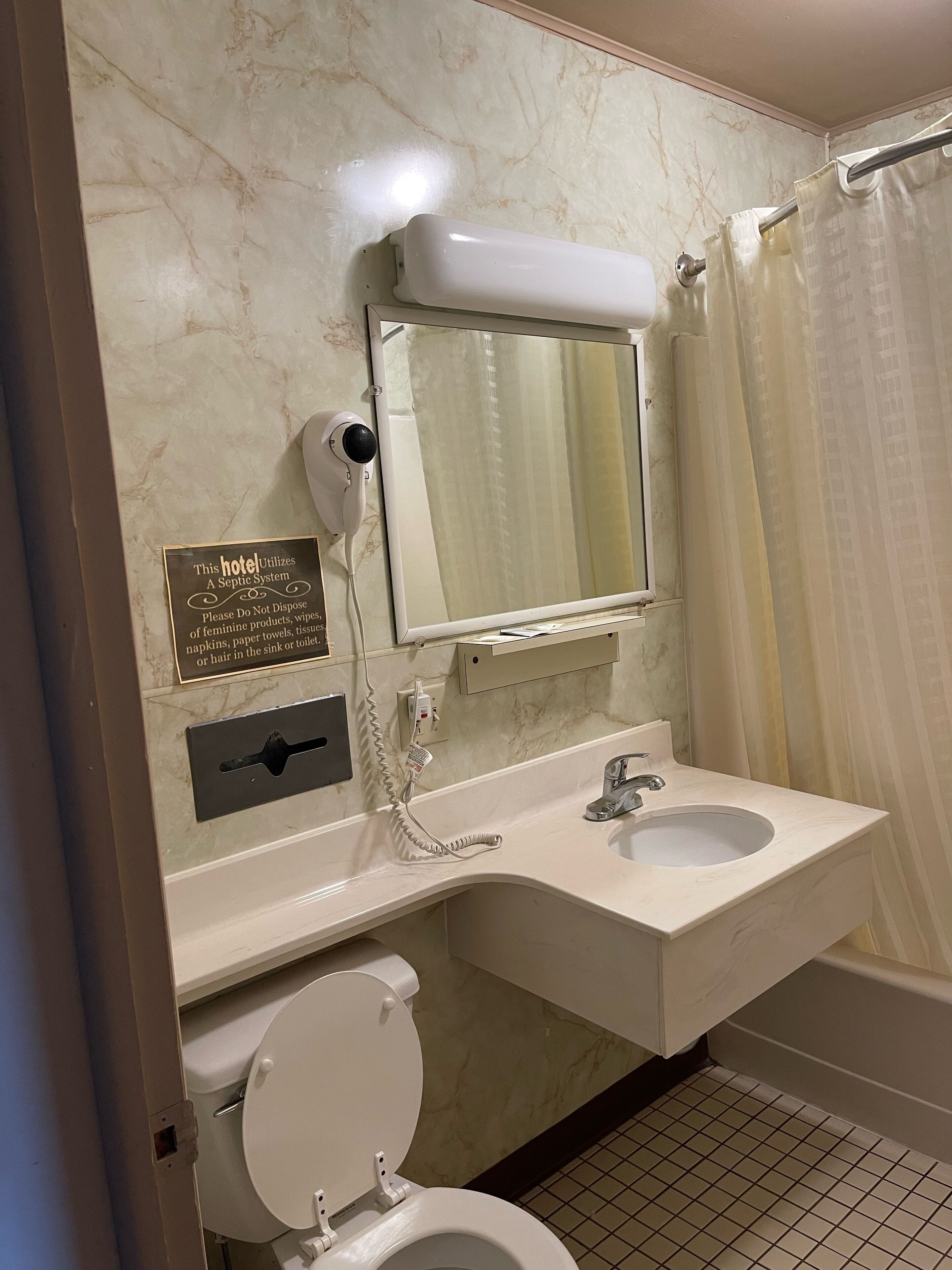 A bathroom with a sink, mirror, and toilet. There is a sign about a septic system.