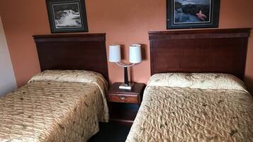 A hotel room with two beds, a nightstand with a lamp, and framed pictures on the wall.