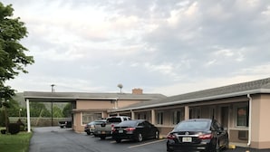 Un estacionamiento con varios autos estacionados frente a un edificio con acceso cubierto.
