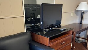 Una habitación con un sofá de cuero negro, un escritorio de madera con una lámpara y un televisor sobre un mueble de madera.