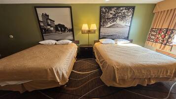 Habitación de hotel con dos camas, una mesita de noche con lámparas, un cuadro en la pared y una alfombra estampada.