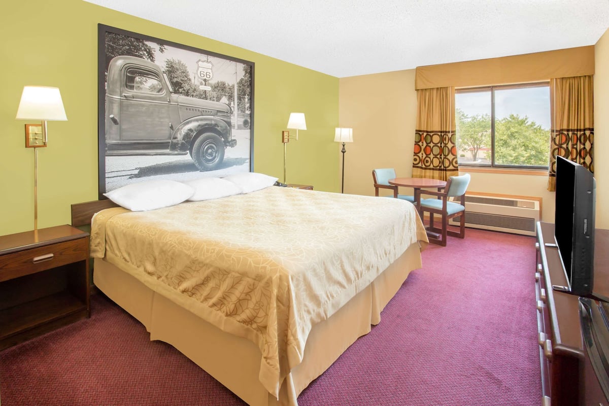 A hotel room with a large bed, a desk, a chair, a television, and a window with curtains.