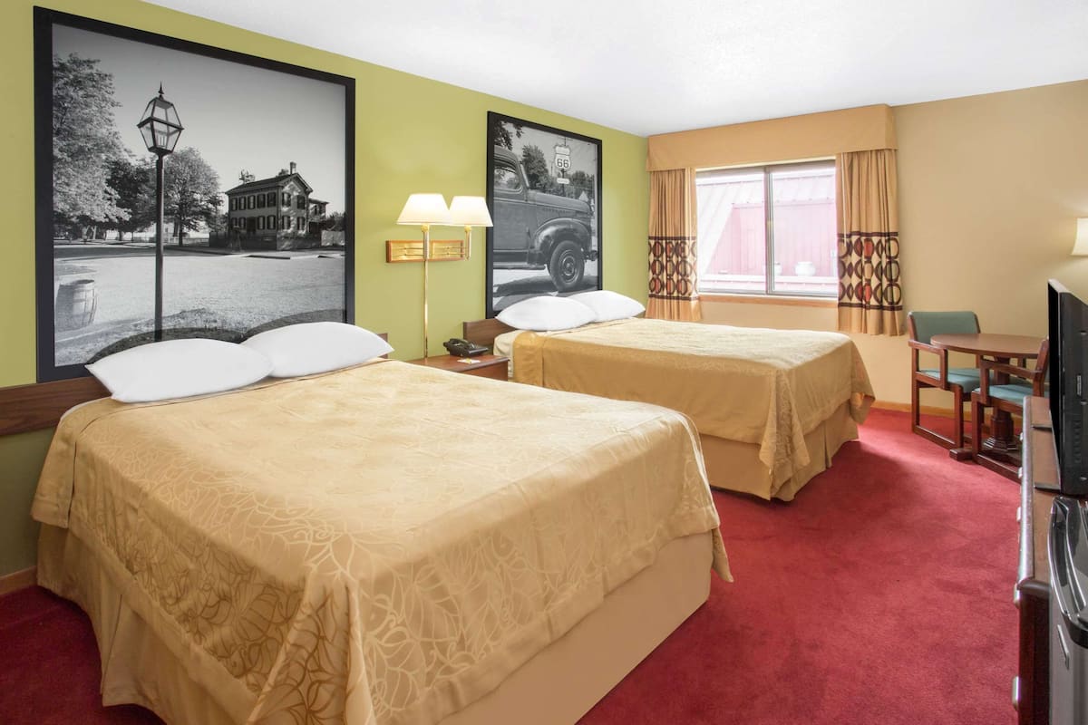 A hotel room with two beds, a desk, a television, and two framed pictures on the wall.