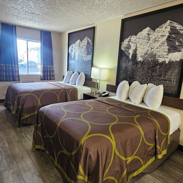 A hotel room with two beds, a large window with curtains, and mountain landscape paintings on the walls.
