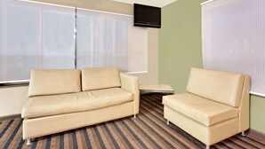 A hotel room with a beige sofa, a small table, and a TV mounted on the wall.