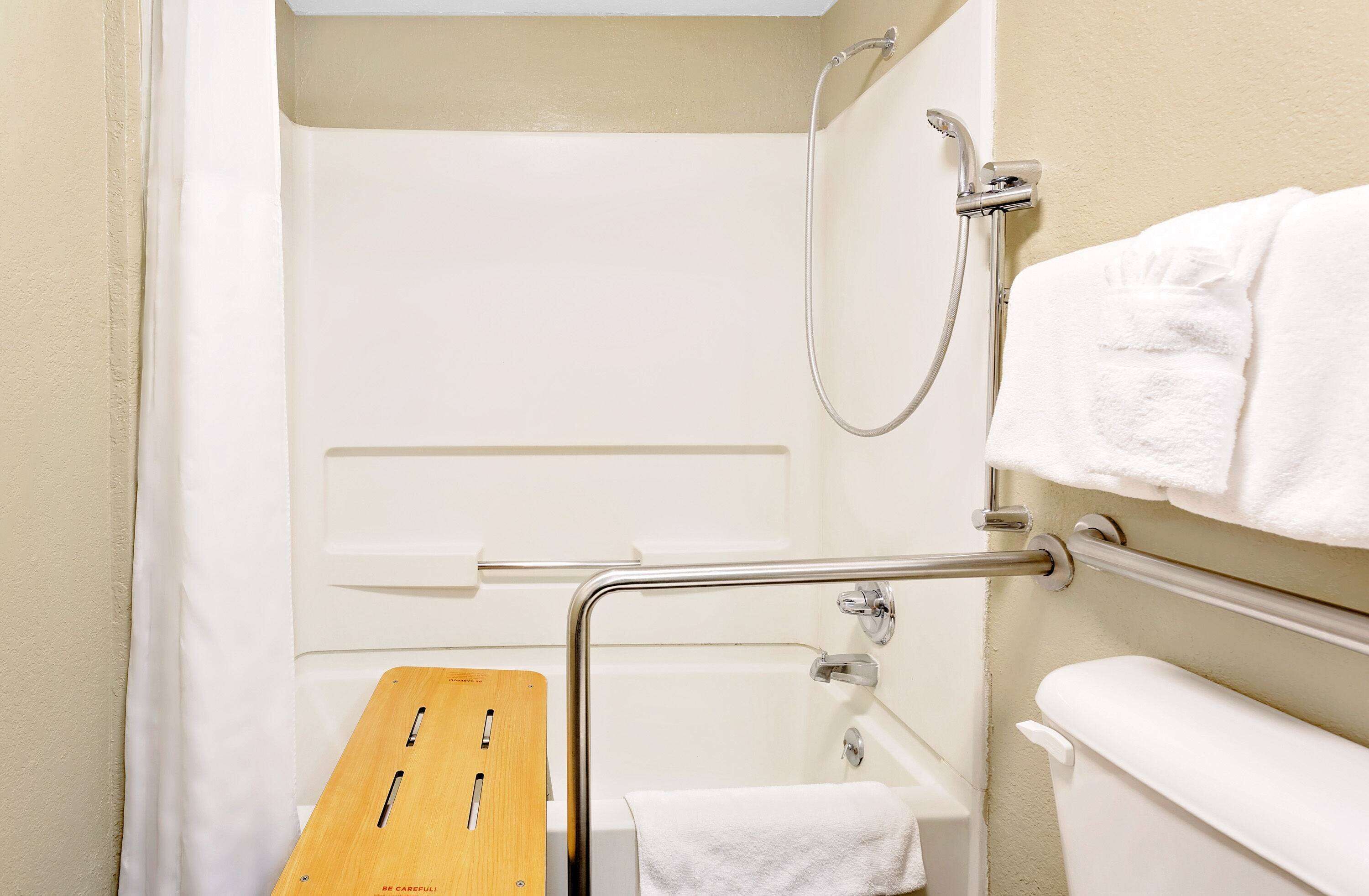 A bathroom with a shower, a grab bar, a wooden bench, and a towel rack.