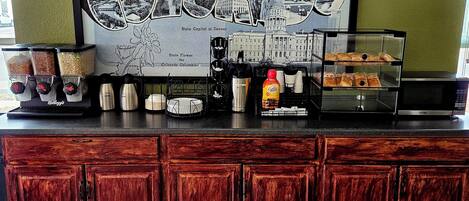 A counter with a large framed sign reading "Greetings from Denver" and "State Capital in Denver," coffee machines, a coffee dispenser, and a display case with pastries.