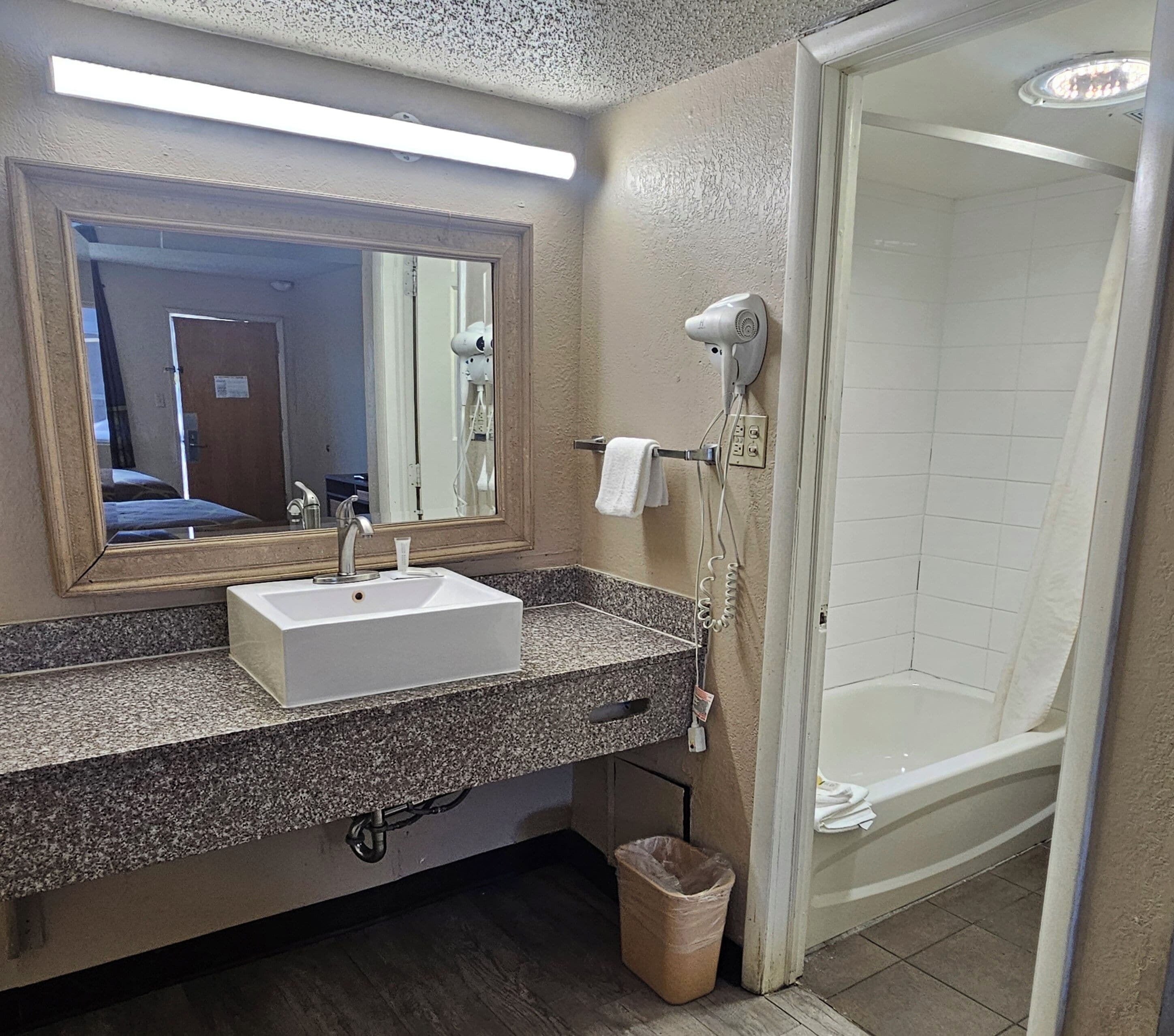 A bathroom with a sink, mirror, hairdryer, and shower.