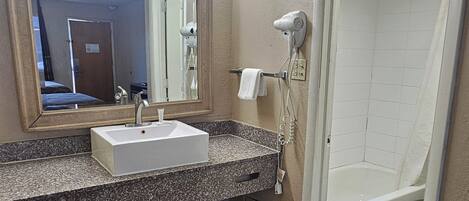 A bathroom with a sink, mirror, hairdryer, and shower.