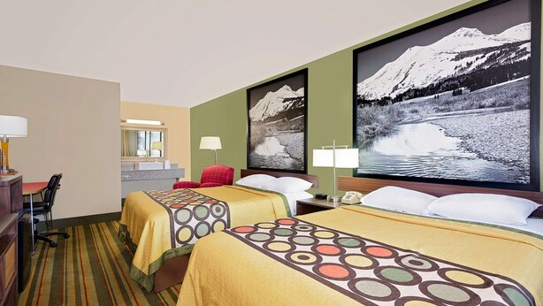 A hotel room with two beds, a desk, and a chair. There are two large framed pictures on the wall.