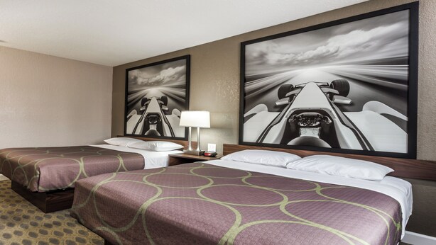 A hotel room with two beds, a nightstand with a lamp, and two large framed pictures on the wall. - Deluxe Inn Willows (Willows)