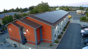 A building with a flat roof and solar panels, a parking lot, and a street view. - Deluxe Inn Willows (Willows)