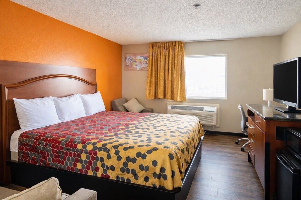 A hotel room with a bed, a desk, a television, and an air conditioning unit.