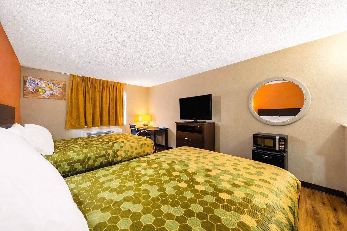 A hotel room with two beds, a desk, a television, a mirror, and a microwave.