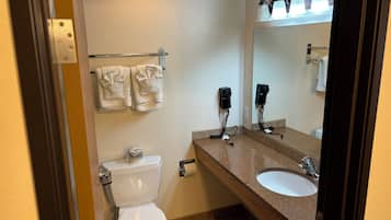 Un baño con inodoro, lavamanos y espejo. Hay toallas colgadas en un perchero y un secador de pelo en la pared.