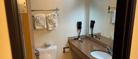 A bathroom with a toilet, sink, and mirror. There are towels hanging on a rack and a hairdryer on the wall.