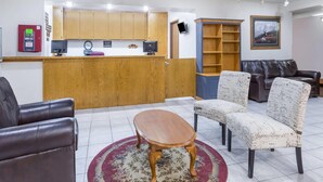 Un vestíbulo de hotel con mostrador de recepción, armarios de madera, un televisor, una estantería, sofás de cuero y una alfombra estampada.