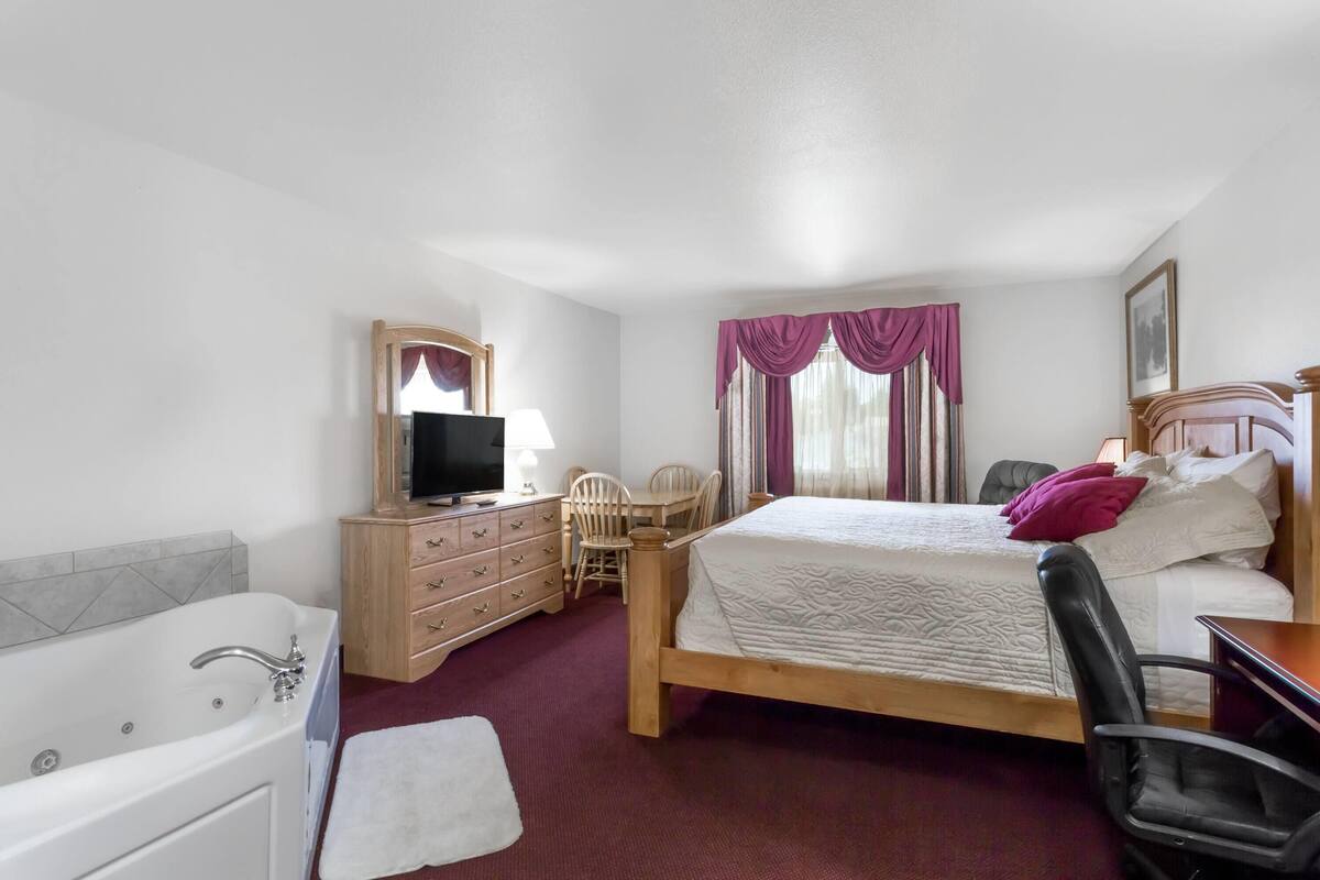 Une chambre à coucher avec un grand lit, une commode en bois, une télévision, un bureau et une chaise.