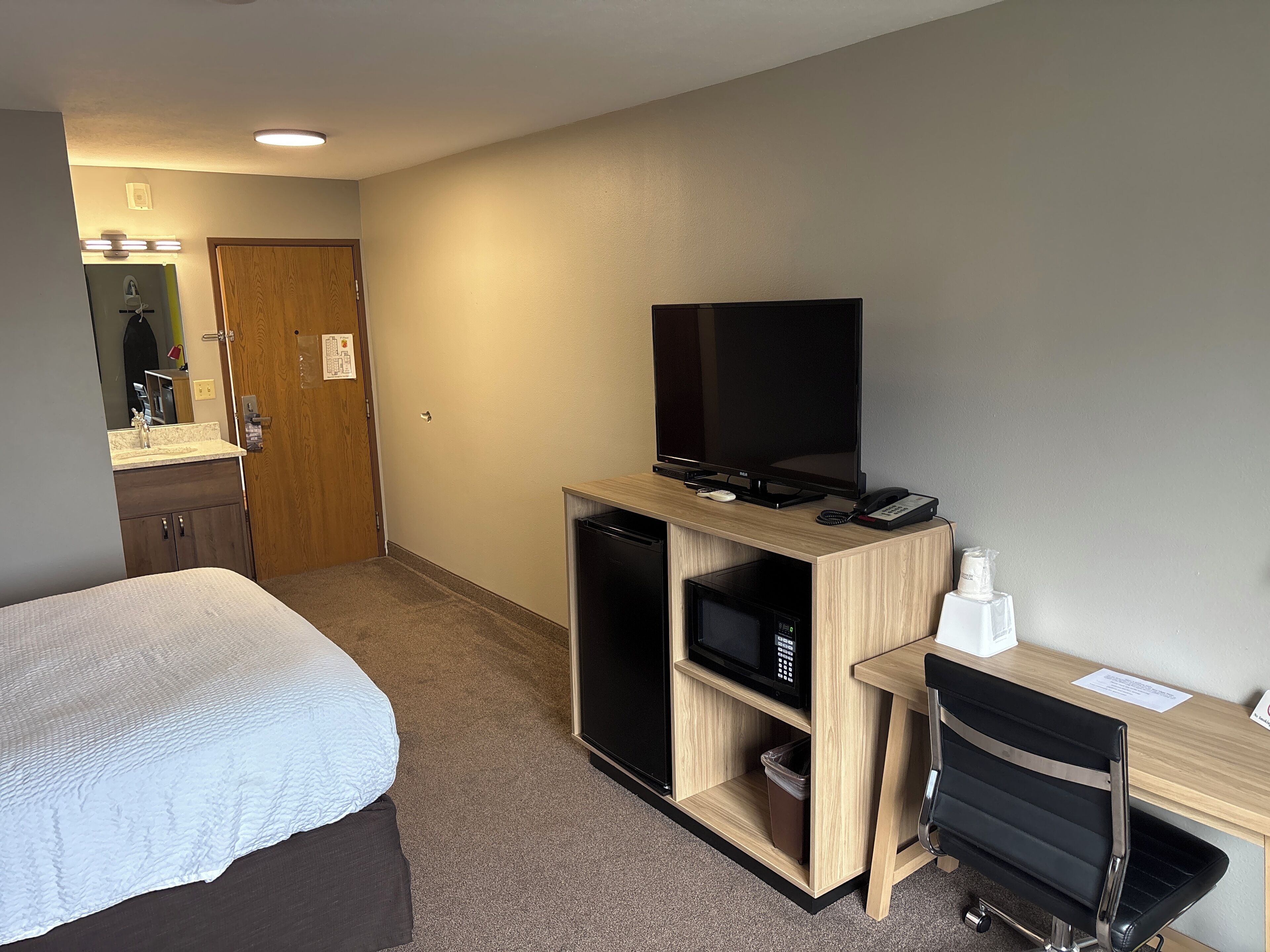 A hotel room with a bed, a desk with a computer, a television, a trash bin, and a mirror.