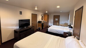 Habitación de hotel con dos camas, televisión, escritorio, espejo y baño.