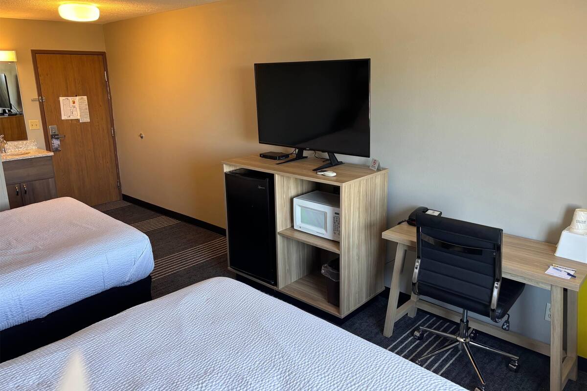 Une chambre d’hôtel avec deux lits, un bureau avec un ordinateur, une télévision, un four à micro-ondes et un petit réfrigérateur.