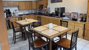 Una cocina con armarios de madera, una mesa de comedor con sillas, un microondas, una cafetera y un refrigerador.