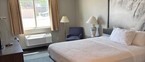 A hotel room with a large bed, two bedside lamps, a chair, a desk with a lamp, and a large window with curtains.