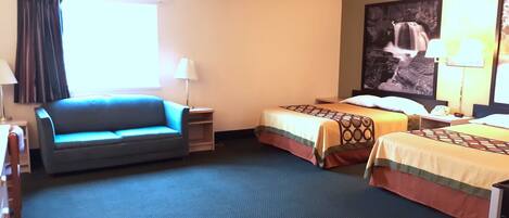 Habitación de hotel con sofá, dos camas individuales, escritorio, lámpara y un cuadro grande en la pared.