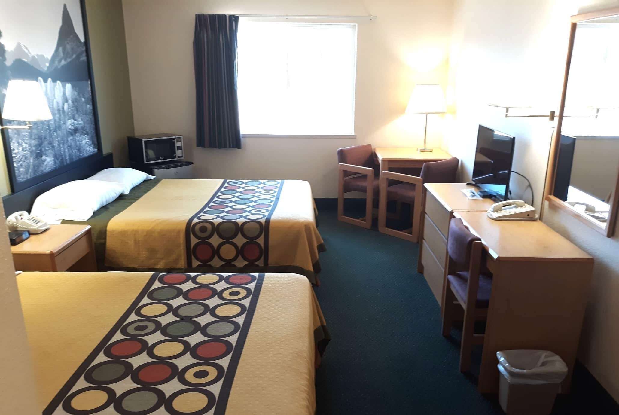 A hotel room with two beds, a desk, a chair, a TV, a lamp, and a window with curtains.