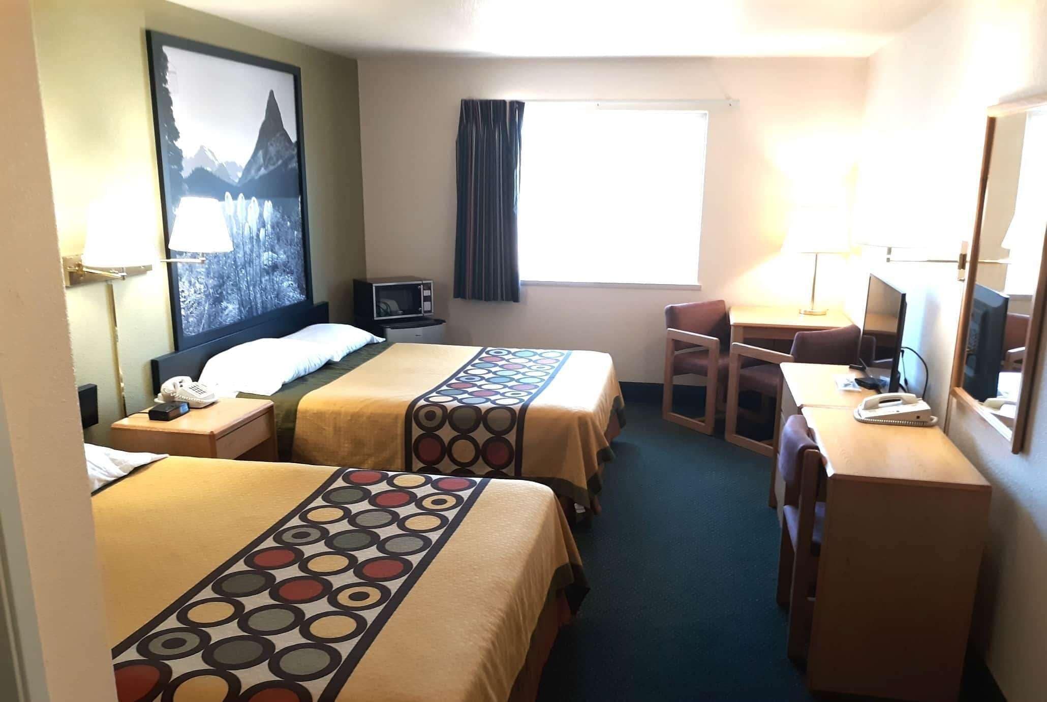 A hotel room with two beds, a desk, a chair, a TV, and a window with curtains.