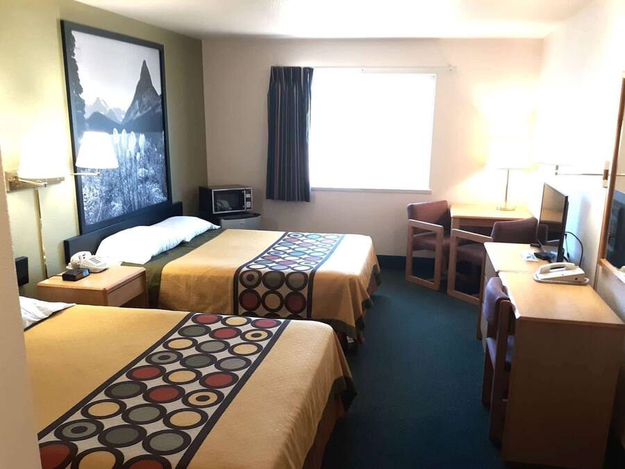 A hotel room with two beds, a desk, a chair, a TV, and a window with curtains.