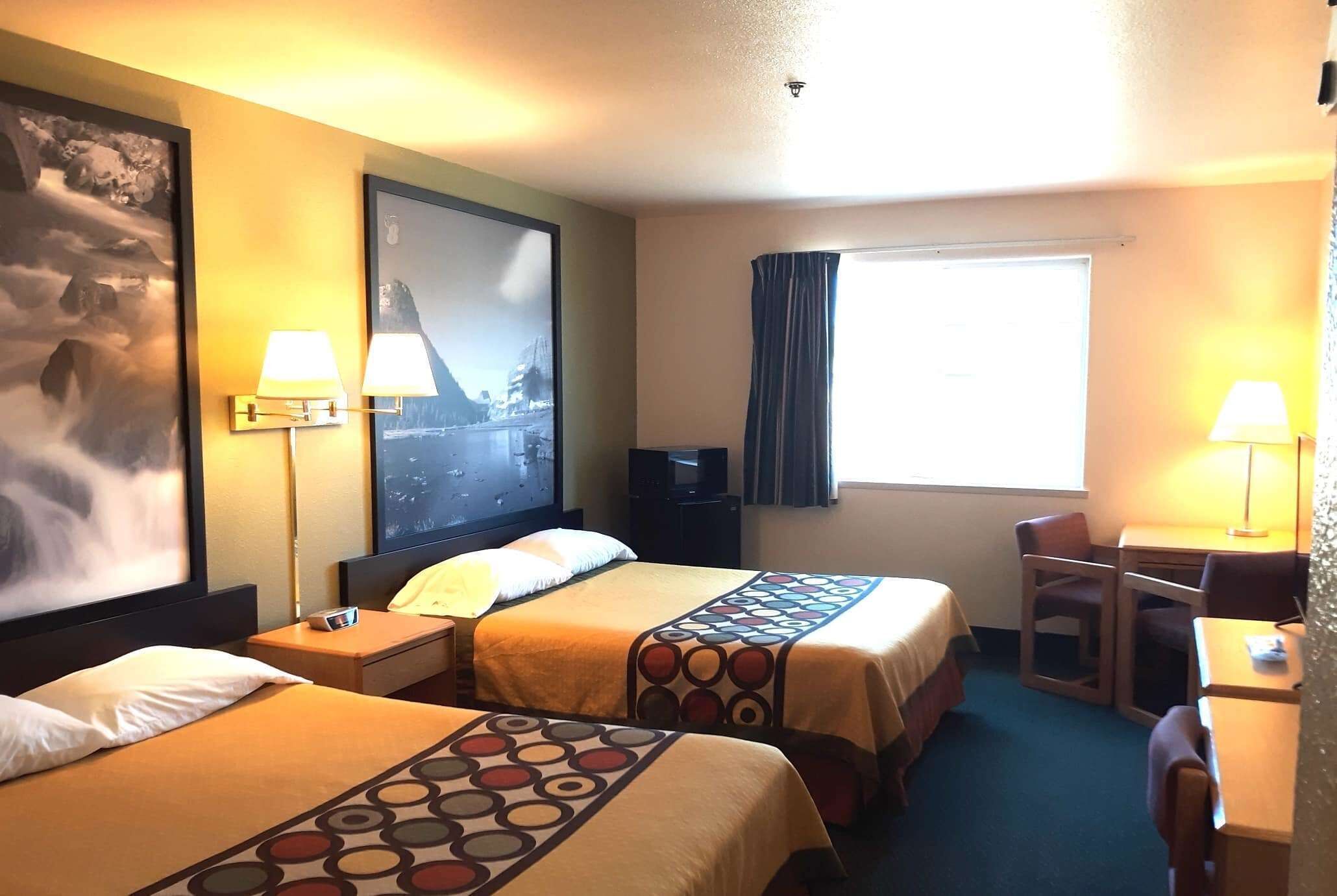 Une chambre d’hôtel avec deux lits, un bureau, une chaise, une télévision et une grande fenêtre avec des rideaux.