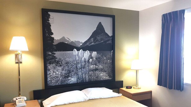 A hotel room with a bed, two bedside lamps, a telephone, a framed picture of a mountain landscape, and a window with curtains. - Hotel Hamilton (Hamilton)