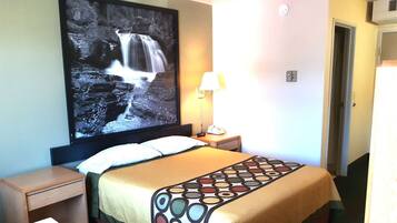 Una habitación de hotel con una cama, una mesita de noche, un televisor en la pared mostrando una cascada y una lámpara.