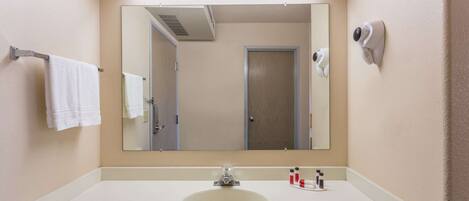Une salle de bain avec un lavabo blanc, un miroir, un porte-serviettes, un sèche-cheveux et une porte.