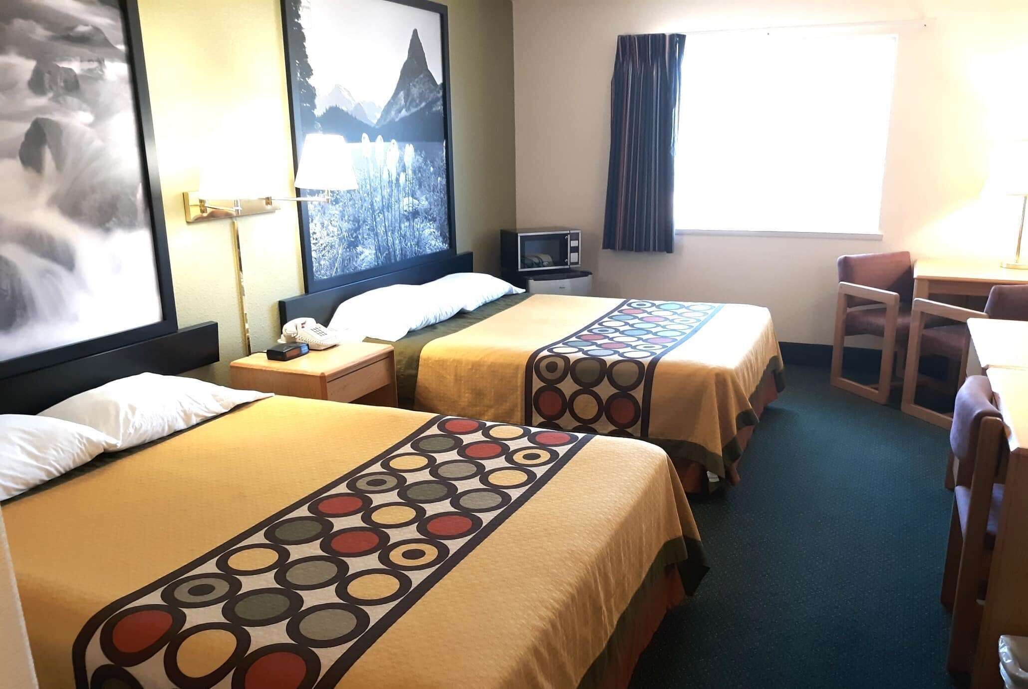 Een hotelkamer met twee bedden, een bureau, een stoel, een televisie en een raam met gordijnen.