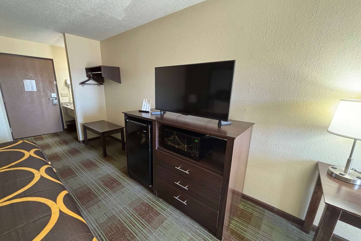 A hotel room with a bed, a flat-screen TV, a microwave, and a small table.