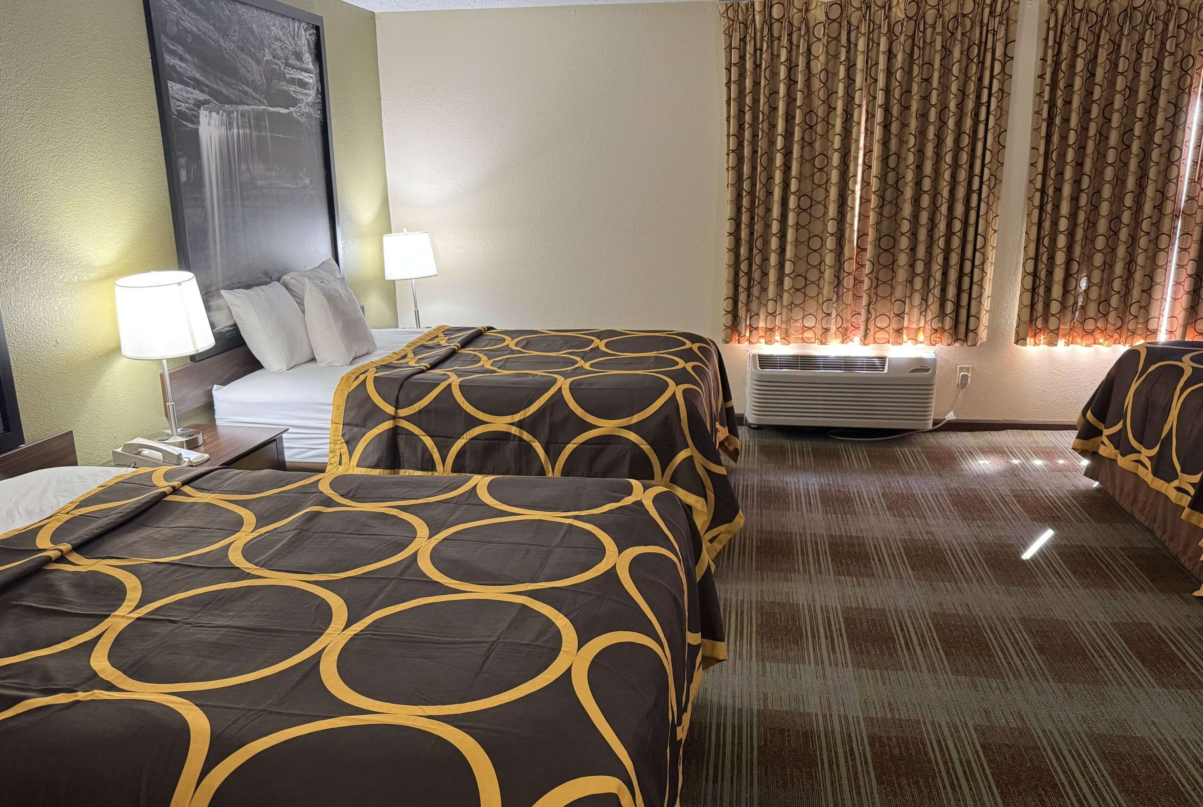 Habitación de hotel con dos camas, un cuadro grande en la pared, una ventana con cortinas y piso alfombrado.