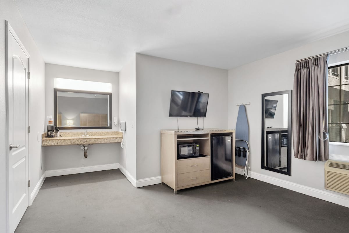 A hotel room with a large mirror, a flat-screen TV, a microwave, a mini-fridge, and a surfboard.