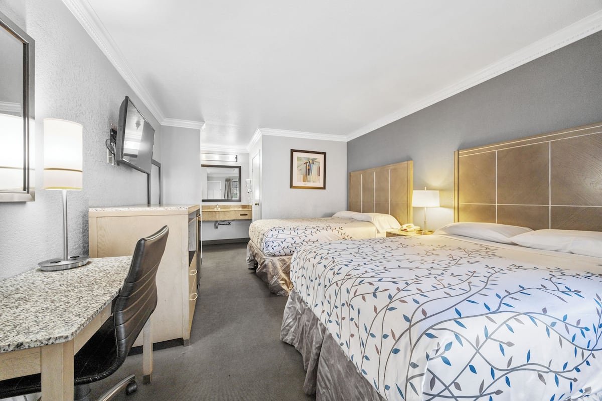 A hotel room with a desk, two beds, a chair, and a TV.