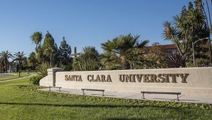 Schild der Santa Clara University mit einem Kreuz und Palmen im Hintergrund.