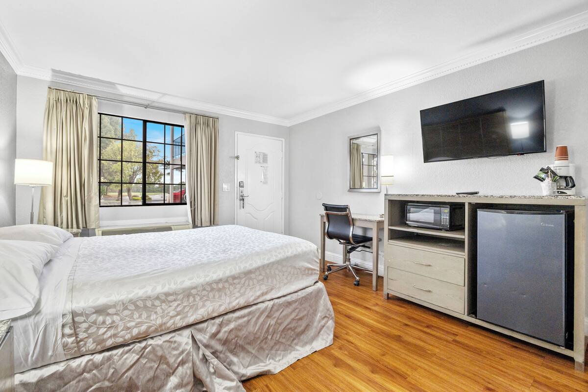 A hotel room with a bed, a desk with a computer, a television, and a refrigerator.