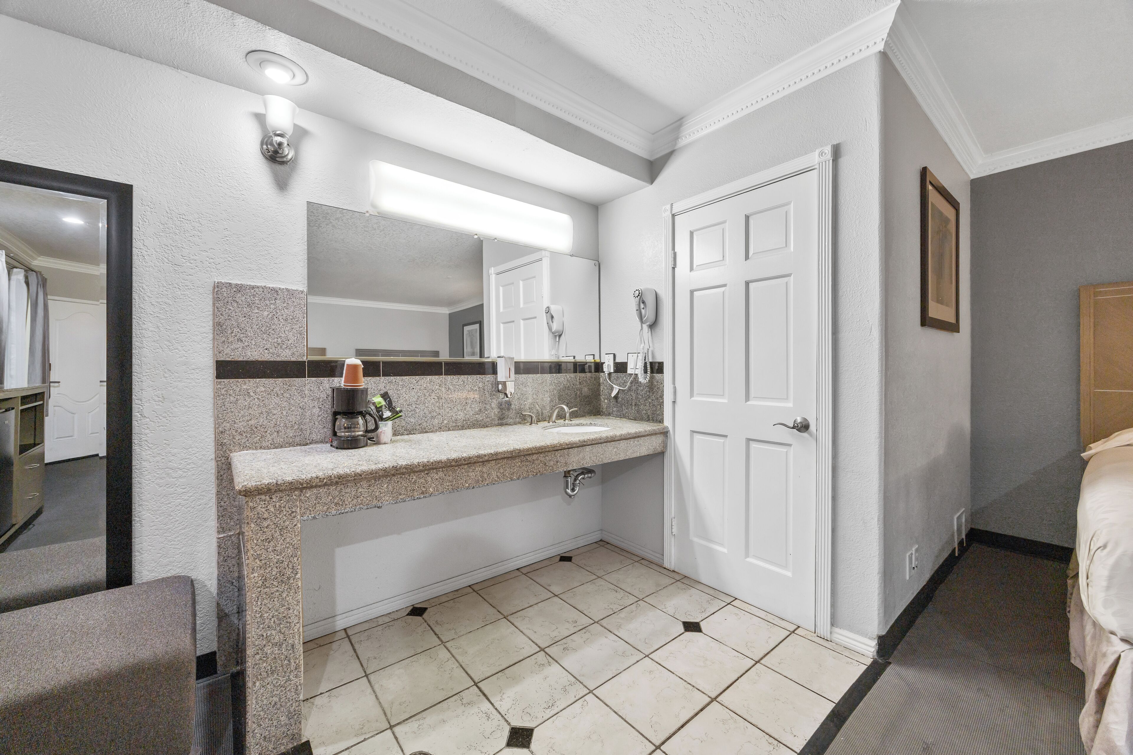 A modern bathroom with a granite countertop, a large mirror, a white door, and a tiled floor.