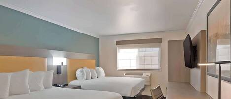 A hotel room with two beds, a desk, a chair, a TV, and a window.