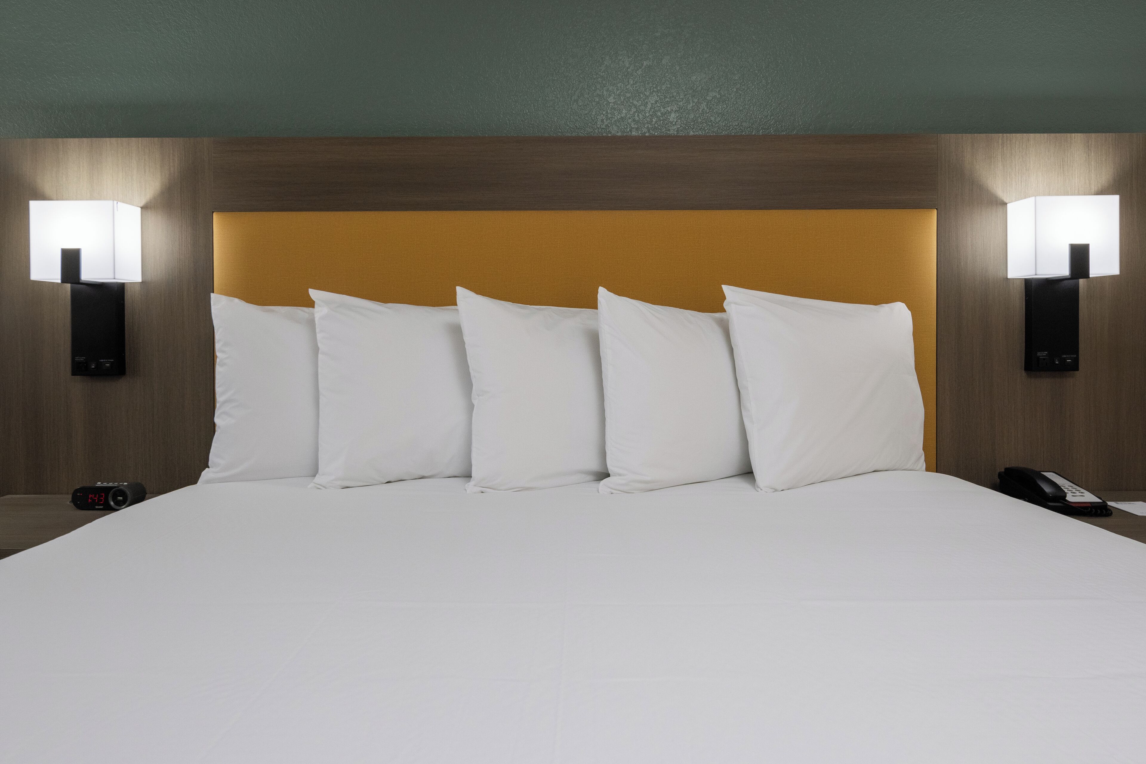 A hotel room with a large bed, two bedside lamps, a clock, and a phone on the nightstand.