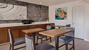 A modern kitchen with a built-in microwave, wooden cabinets, and a marble backsplash. There are two wooden tables with chairs, and a white door in the background. - Comfort Inn Hayward - Oakland South (Hayward)