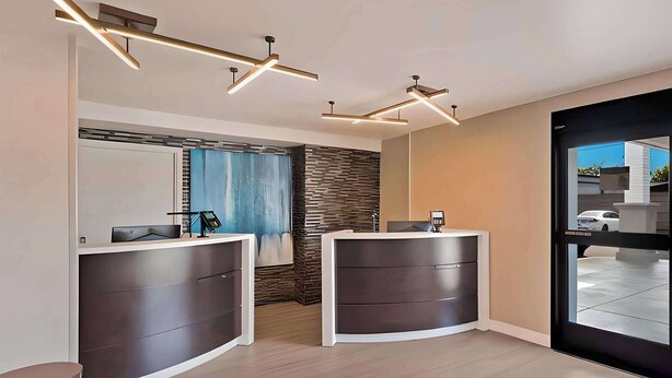 A reception area with two dark-colored reception desks, a blue curtain, a stone wall, and modern lighting fixtures. - Comfort Inn Hayward - Oakland South (Hayward)
