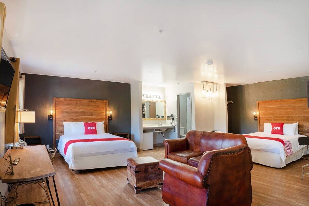 A hotel room with two beds, a leather armchair, a wooden desk, and a mirror.