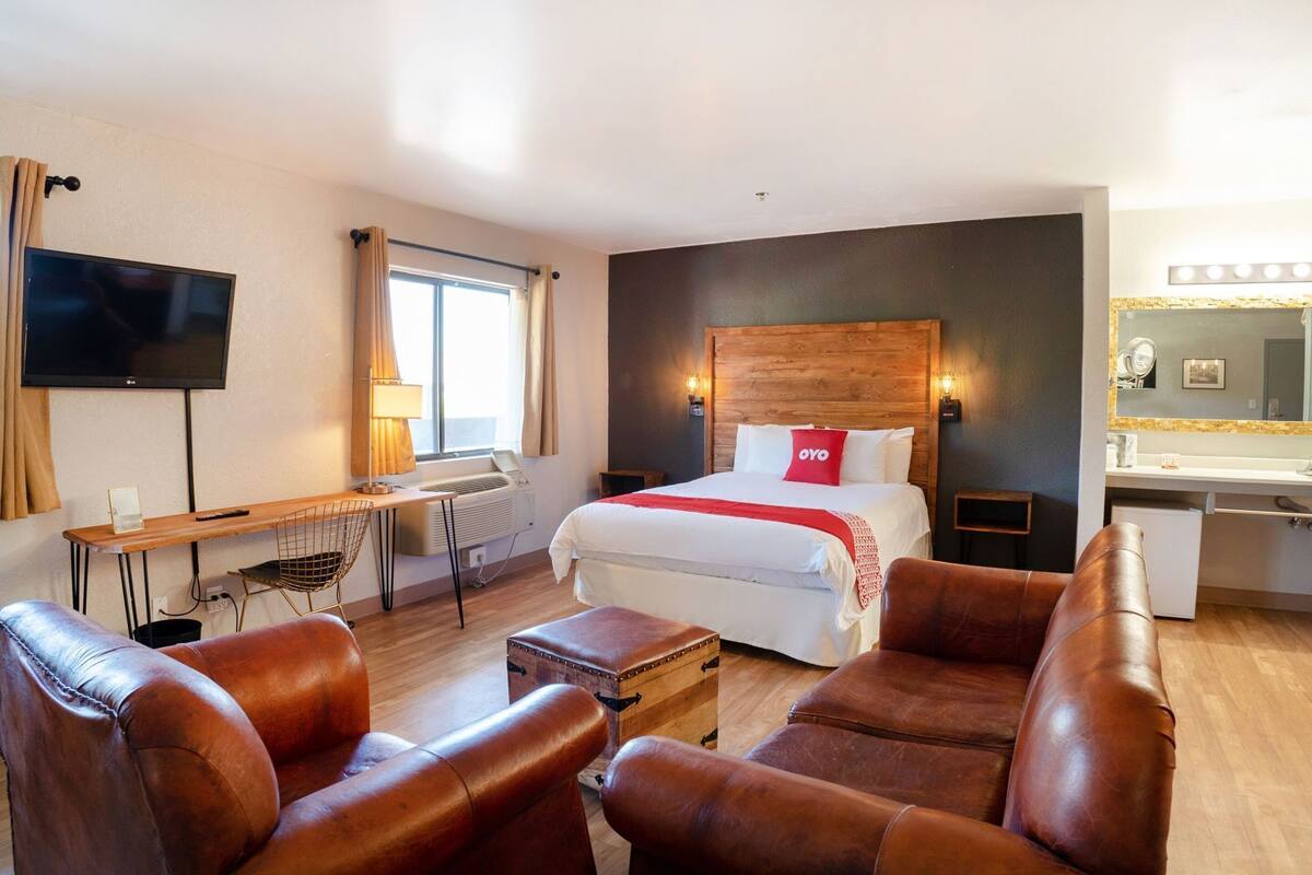 A hotel room with a bed, a desk, a chair, a TV, and a bathroom with a mirror.