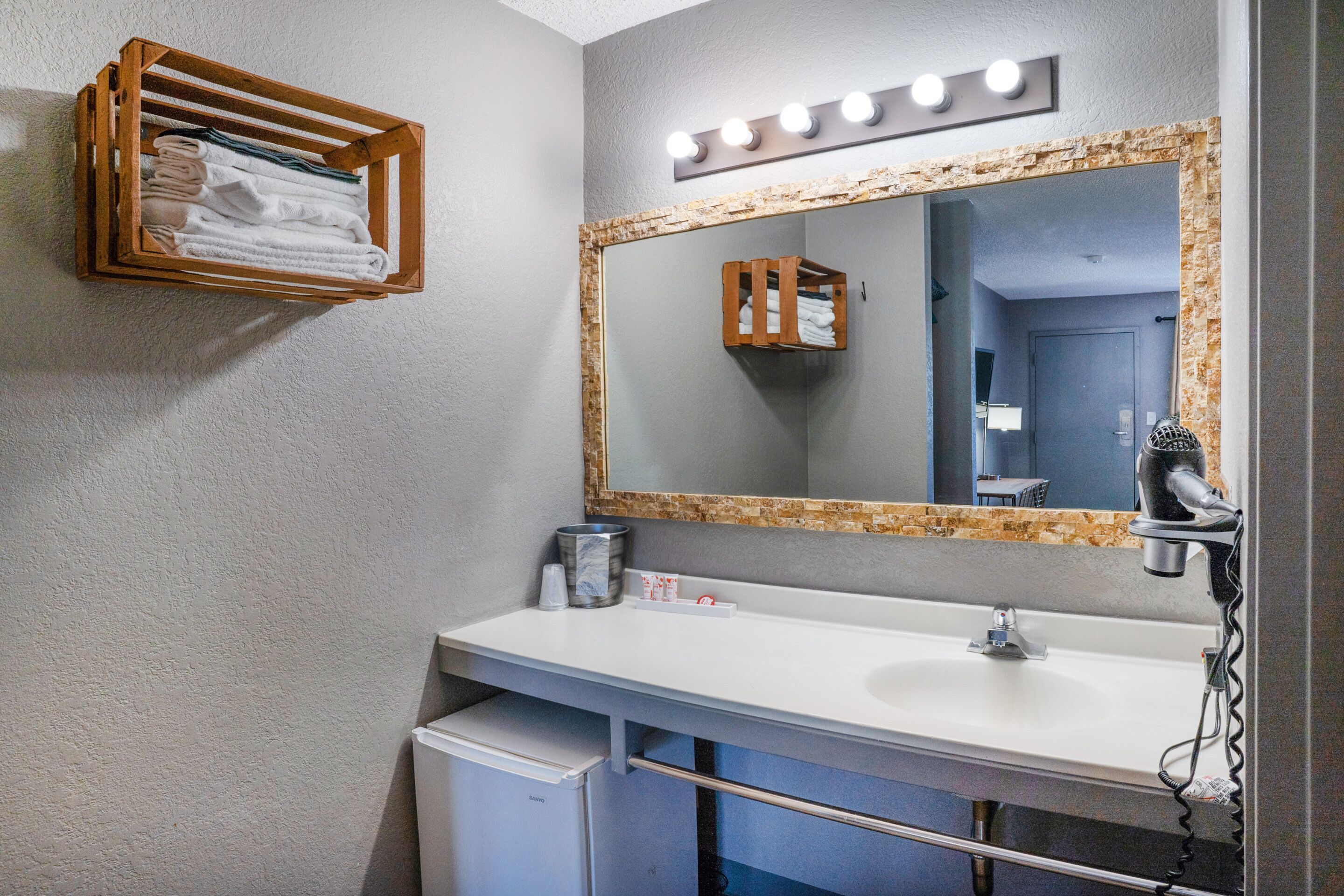 Une salle de bain avec un lavabo blanc, un miroir avec éclairage intégré, un porte-serviettes et un sèche-cheveux.